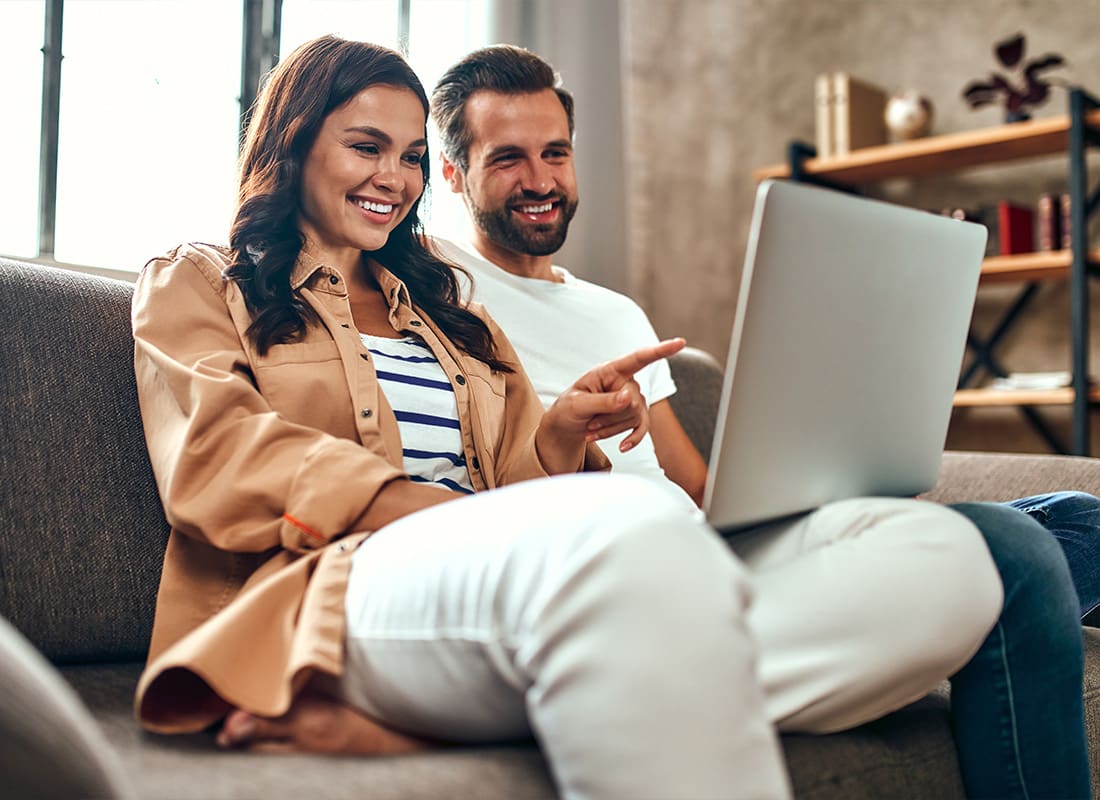 About Our Agency - Young Couple in Love Are Sitting on the Couch With a Laptop at Home