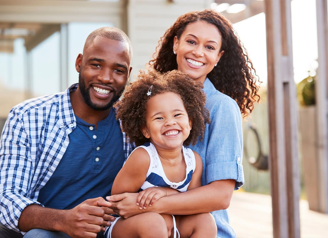 Insurance Solutions - Young Family Embracing Outdoors and Smiling at Camera