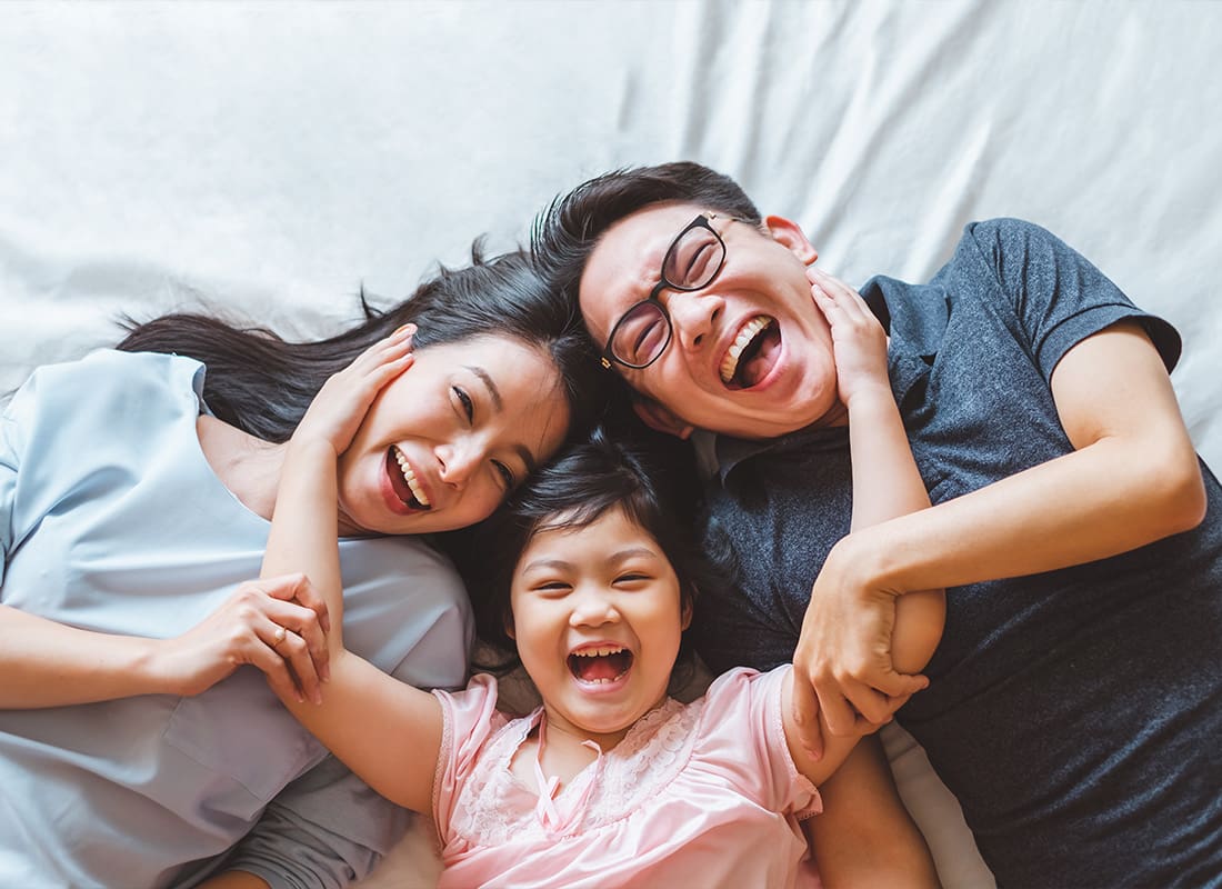 Personal Insurance - Happy Young Family Laying On Bed While Smiling
